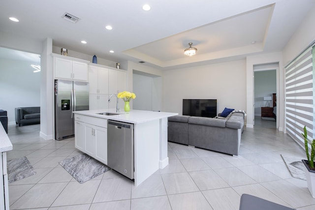 kitchen with appliances with stainless steel finishes, sink, white cabinets, a kitchen island with sink, and a raised ceiling