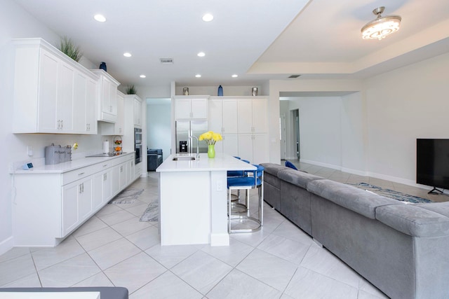 kitchen with white cabinets, an island with sink, a tray ceiling, and a kitchen breakfast bar