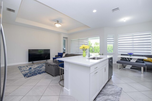 kitchen with a kitchen island with sink, white cabinets, sink, and a raised ceiling