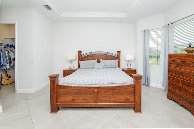 tiled bedroom featuring a raised ceiling and a walk in closet