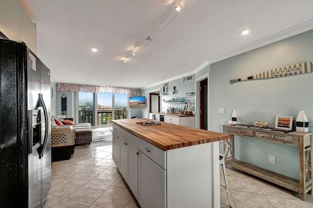 kitchen with a kitchen island, wood counters, a kitchen bar, light tile patterned floors, and black fridge