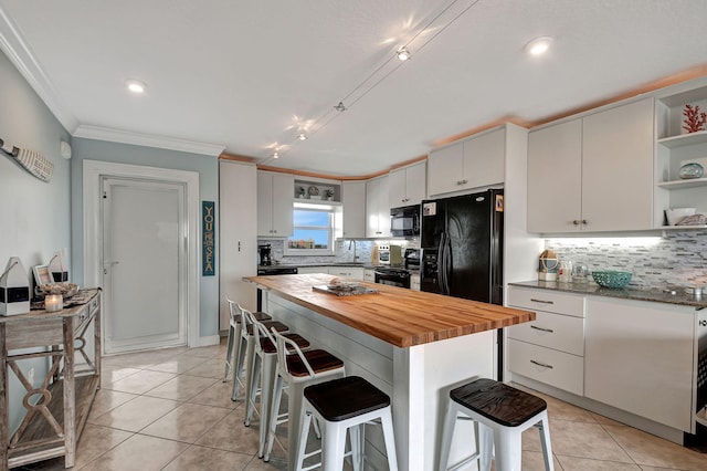 kitchen with wood counters, a breakfast bar area, white cabinets, a center island, and black appliances