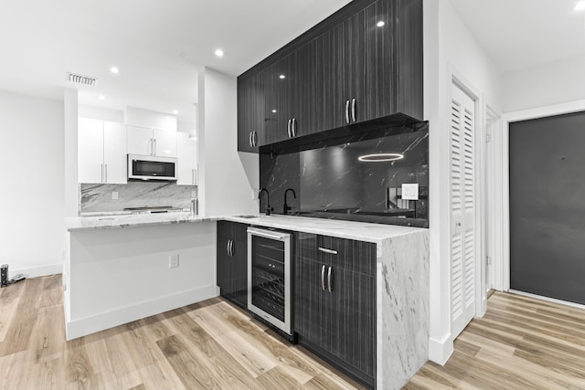 kitchen featuring beverage cooler, visible vents, white cabinets, white microwave, and dark cabinets