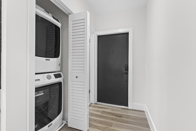 washroom featuring baseboards, laundry area, light wood-type flooring, and stacked washer / drying machine