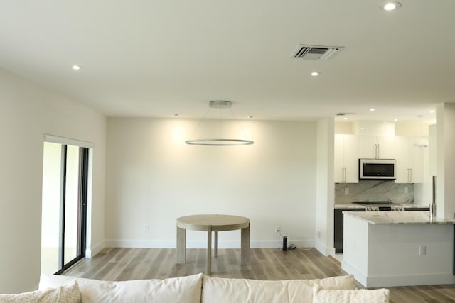 kitchen featuring visible vents, white cabinets, decorative backsplash, white microwave, and light stone countertops