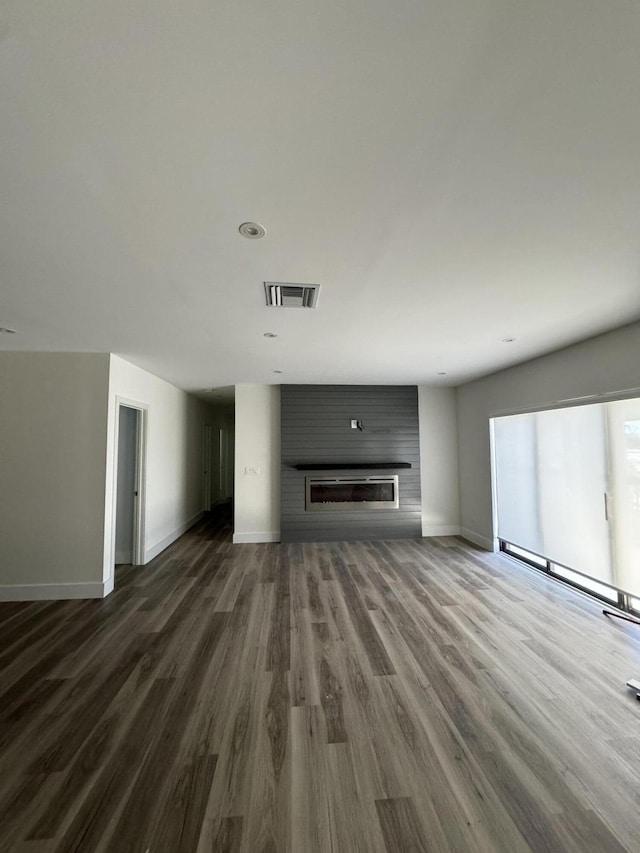 unfurnished living room with a large fireplace, dark wood-type flooring, visible vents, and baseboards