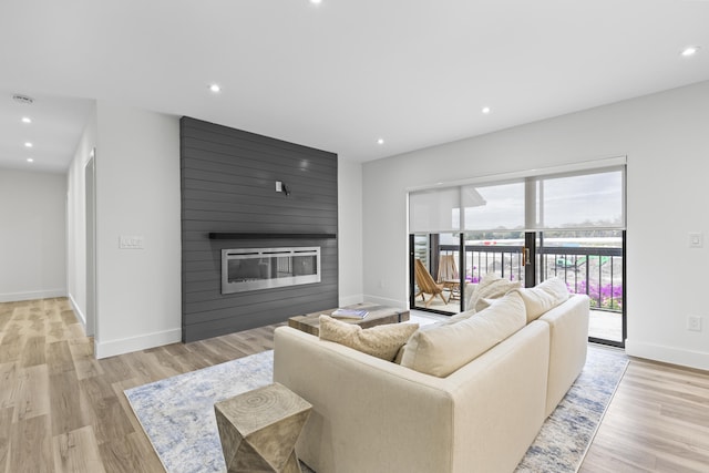 living room featuring light wood-style flooring, a fireplace, baseboards, and recessed lighting