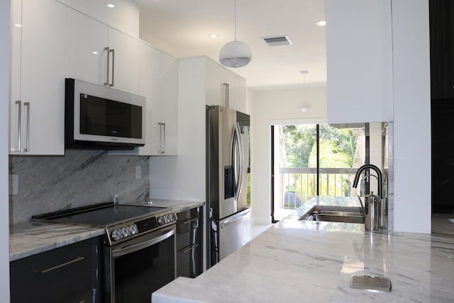 kitchen with light stone countertops, stainless steel appliances, white cabinetry, pendant lighting, and a sink