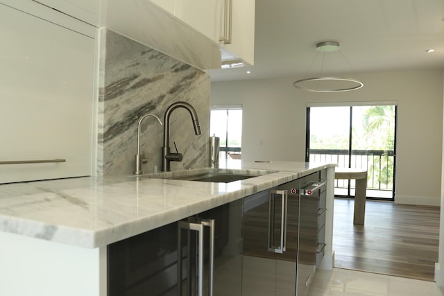 kitchen with wine cooler, a sink, baseboards, dark cabinetry, and light stone countertops