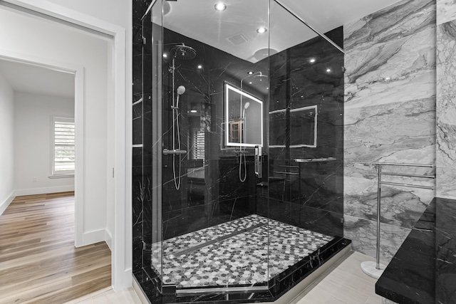 full bath featuring visible vents, wood finished floors, a marble finish shower, and baseboards