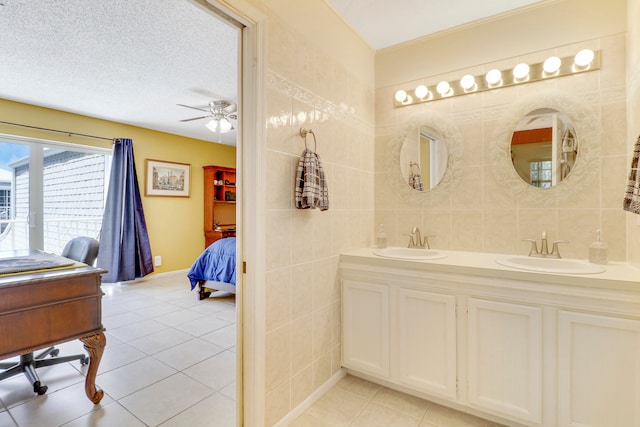 bathroom featuring a textured ceiling, ceiling fan, tile walls, tile patterned flooring, and dual vanity