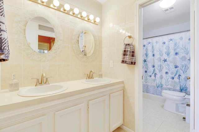 bathroom featuring toilet, tile walls, double sink vanity, backsplash, and tile patterned flooring