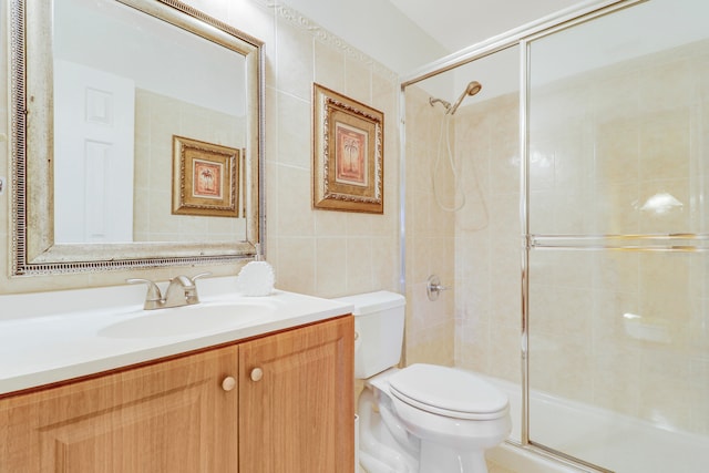 bathroom with tile walls, toilet, vanity, and an enclosed shower