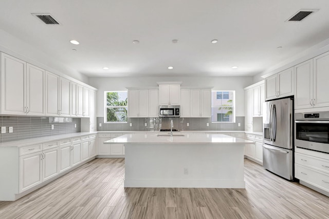 kitchen featuring appliances with stainless steel finishes, white cabinets, and a kitchen island with sink