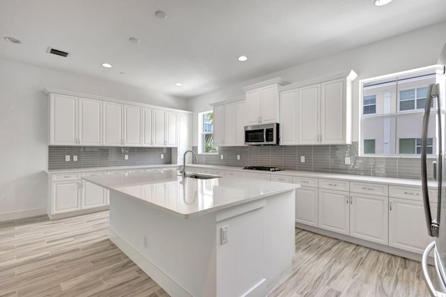 kitchen with decorative backsplash, appliances with stainless steel finishes, a center island with sink, sink, and white cabinetry