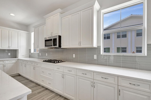 kitchen featuring white cabinets, light wood-type flooring, cooktop, and decorative backsplash