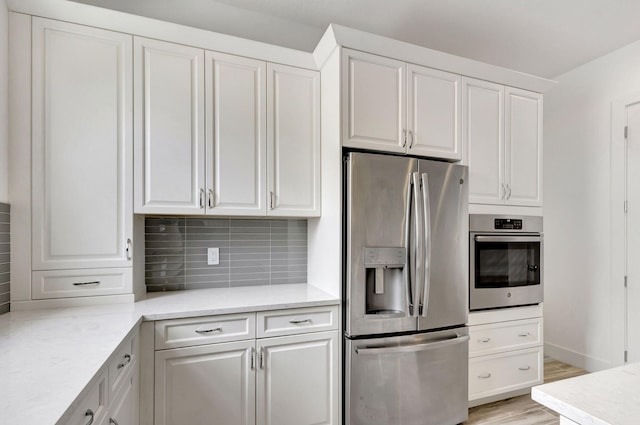 kitchen with white cabinets, light wood-type flooring, stainless steel appliances, and decorative backsplash