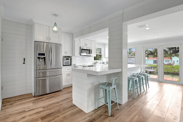 kitchen featuring ornamental molding, appliances with stainless steel finishes, white cabinetry, light wood-style floors, and a kitchen breakfast bar
