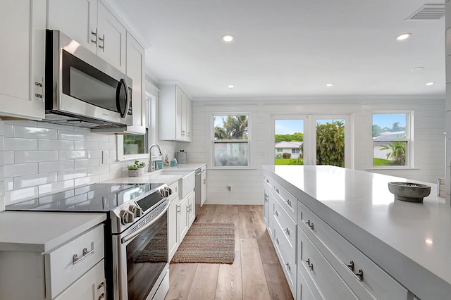 kitchen with appliances with stainless steel finishes, light hardwood / wood-style flooring, a healthy amount of sunlight, and white cabinets