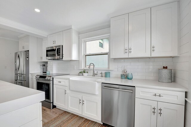 kitchen featuring ornamental molding, stainless steel appliances, decorative backsplash, a sink, and white cabinets