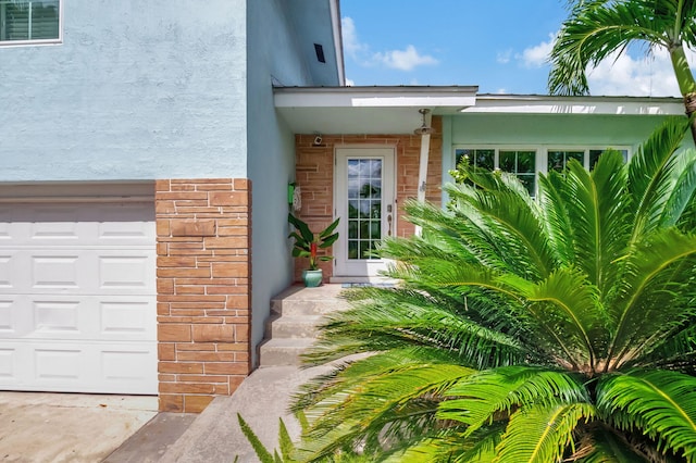 view of exterior entry featuring stucco siding, an attached garage, and stone siding
