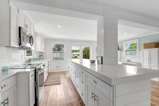 kitchen featuring appliances with stainless steel finishes, backsplash, white cabinetry, ornamental molding, and light wood-type flooring