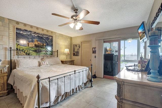 tiled bedroom with access to exterior, a textured ceiling, ceiling fan, and tile walls