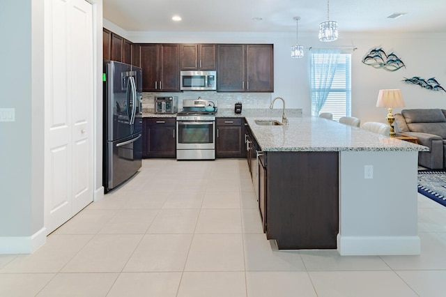 kitchen with pendant lighting, stainless steel appliances, open floor plan, a sink, and a peninsula