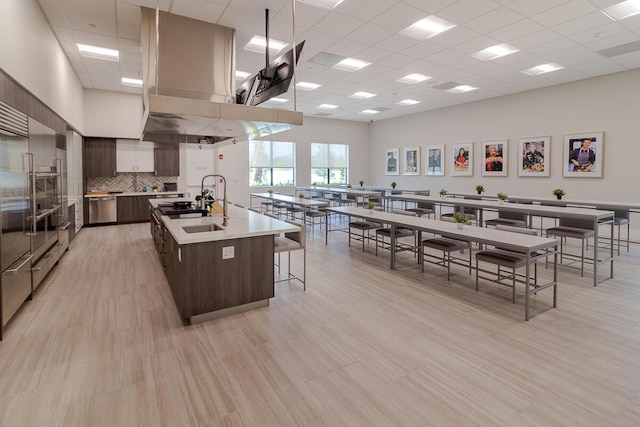 kitchen with light countertops, a towering ceiling, dark brown cabinetry, an island with sink, and modern cabinets