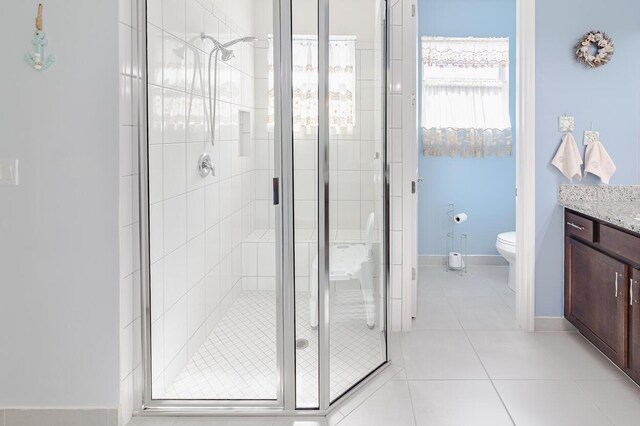 bathroom featuring toilet, a stall shower, vanity, baseboards, and tile patterned floors