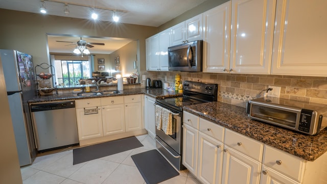 kitchen with dark stone countertops, sink, stainless steel appliances, light tile patterned floors, and white cabinetry