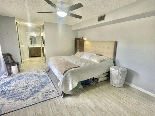 bedroom with ceiling fan, connected bathroom, light hardwood / wood-style floors, and a textured ceiling