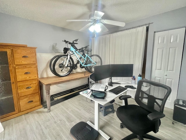 home office with a textured ceiling, ceiling fan, and light wood-type flooring