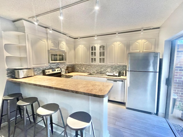 kitchen featuring stainless steel appliances, white cabinetry, kitchen peninsula, a kitchen bar, and tasteful backsplash