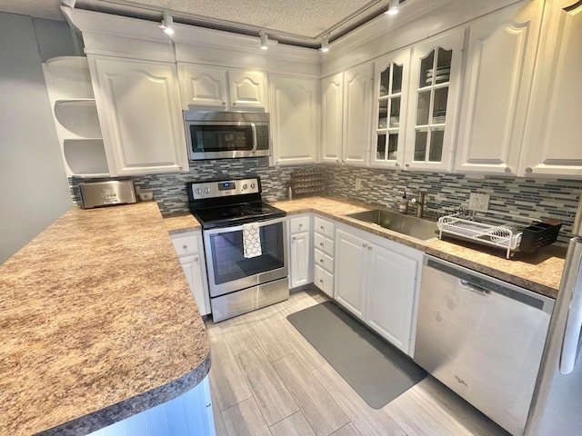 kitchen with light wood-type flooring, tasteful backsplash, sink, appliances with stainless steel finishes, and white cabinets