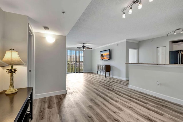 unfurnished living room with ceiling fan, rail lighting, a textured ceiling, and light wood-type flooring