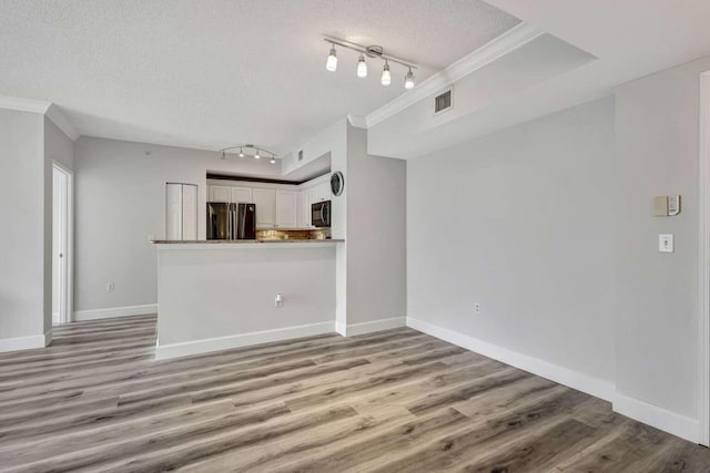 unfurnished living room featuring light wood-type flooring, rail lighting, ornamental molding, and a textured ceiling