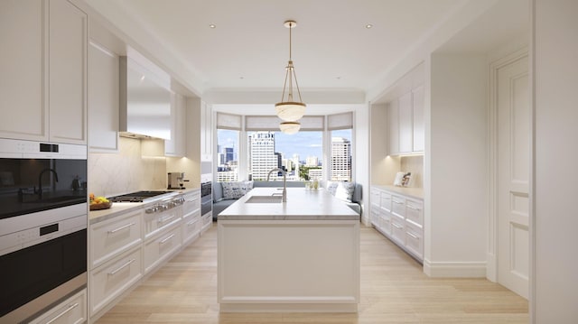 kitchen featuring pendant lighting, a center island with sink, white cabinetry, and sink