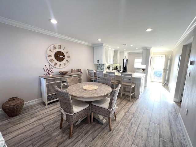 dining space with light hardwood / wood-style flooring, crown molding, and decorative columns