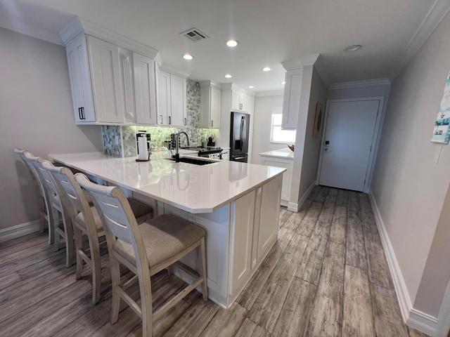 kitchen with backsplash, white cabinetry, light hardwood / wood-style floors, stainless steel fridge with ice dispenser, and kitchen peninsula