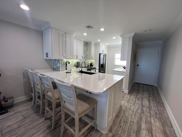 kitchen featuring backsplash, light wood-type flooring, white cabinetry, stainless steel fridge, and kitchen peninsula