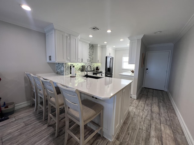 kitchen featuring visible vents, decorative backsplash, white cabinetry, a peninsula, and stainless steel fridge with ice dispenser