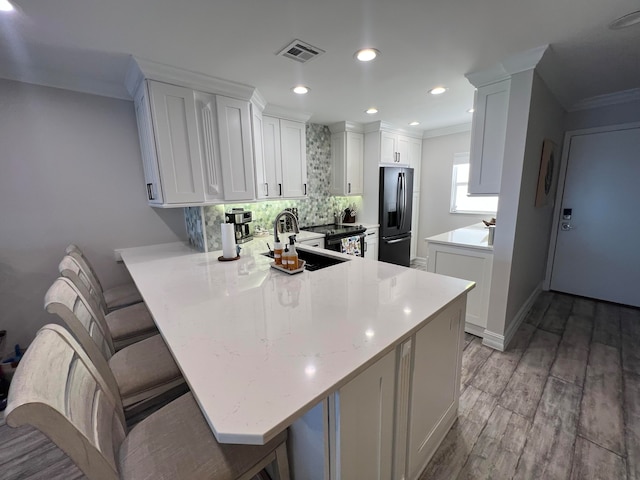 kitchen featuring light wood-type flooring, light stone countertops, tasteful backsplash, stainless steel fridge with ice dispenser, and kitchen peninsula