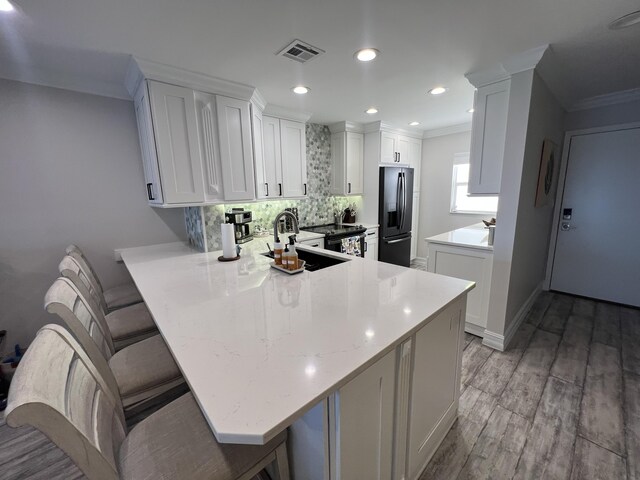 kitchen featuring a peninsula, a sink, visible vents, black fridge, and crown molding