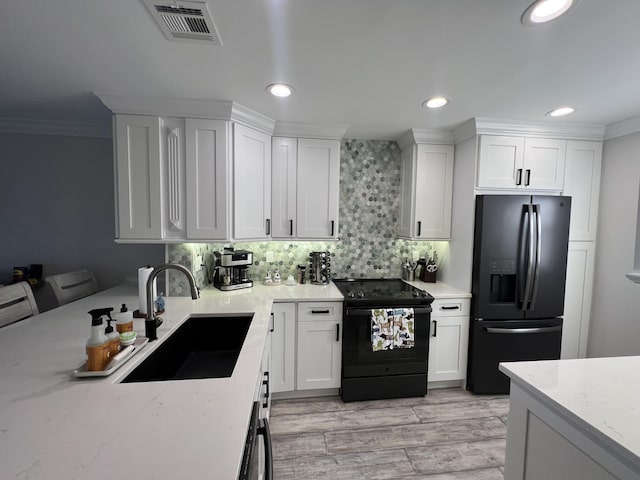 kitchen with visible vents, white cabinets, ornamental molding, black appliances, and a sink