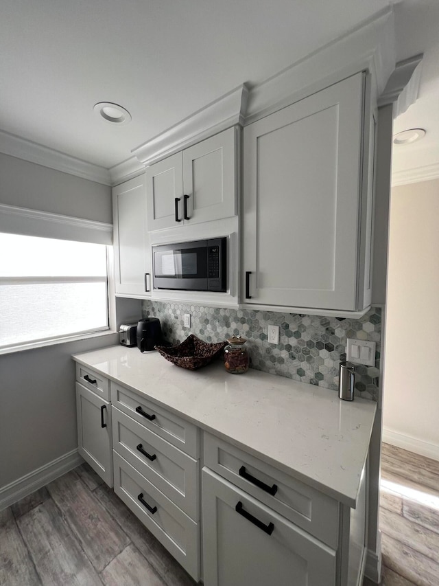 kitchen featuring decorative backsplash, wood-type flooring, built in microwave, light stone countertops, and crown molding