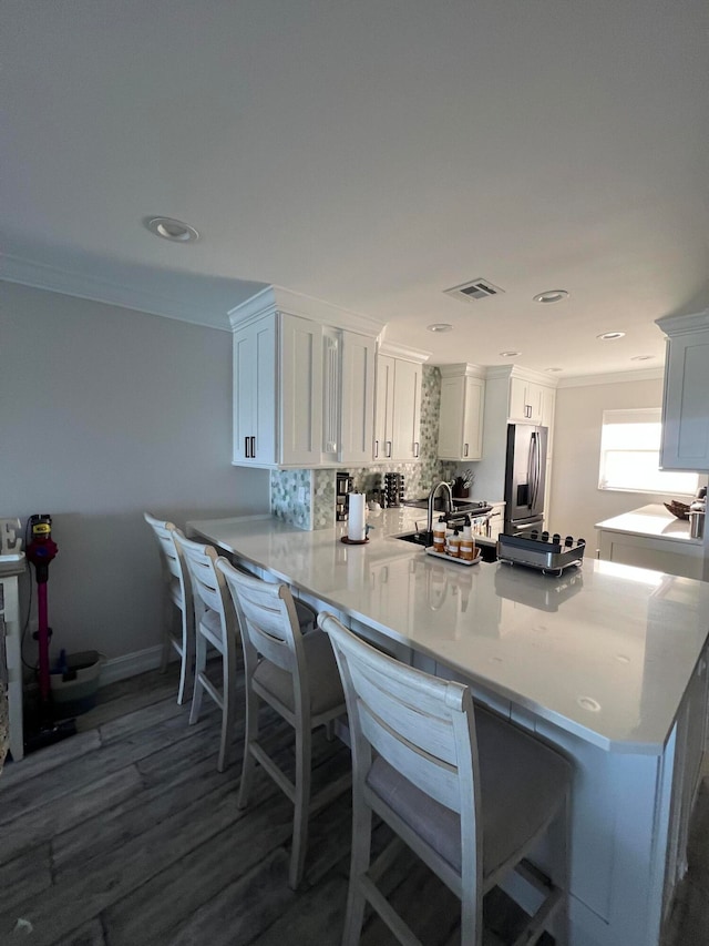 kitchen featuring decorative backsplash, stainless steel refrigerator with ice dispenser, white cabinets, hardwood / wood-style flooring, and kitchen peninsula