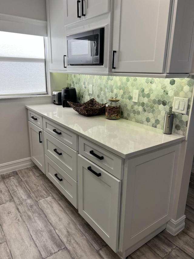 kitchen featuring wood finished floors, baseboards, light countertops, backsplash, and built in microwave