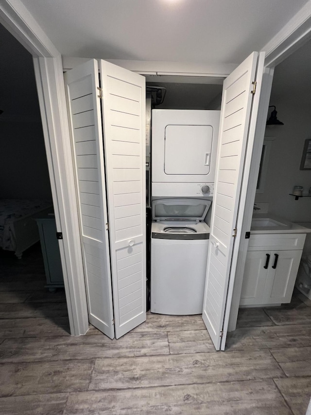 laundry area with a sink, laundry area, stacked washer / dryer, and wood finished floors