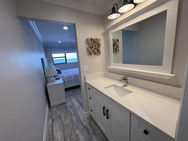 ensuite bathroom with vanity, baseboards, crown molding, and wood finished floors